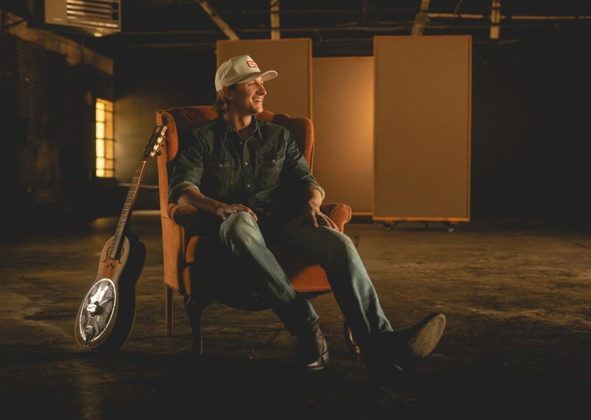 Cooper Alan sat on a chair with a guitar beside himx